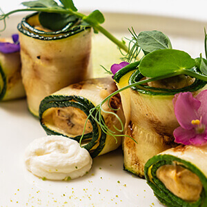 Gegrillte Zucchiniröllchen stapeln sich hübsch dekoriert auf einem Teller